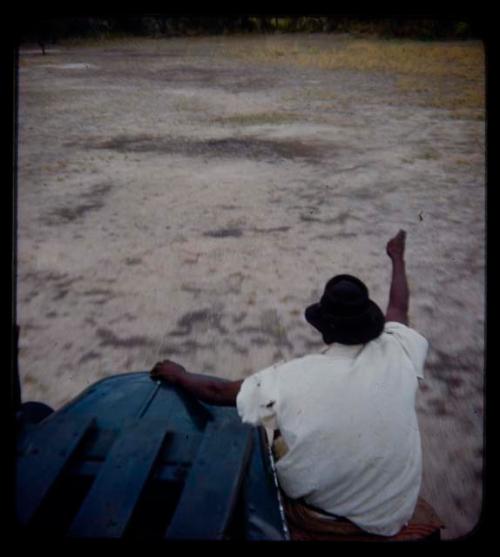 Expedition: Thoria sitting on a truck fender and pointing at something, seen from behind