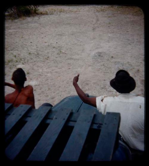 Expedition: Man and Thoria sitting on a truck fender and pointing at something, seen from behind