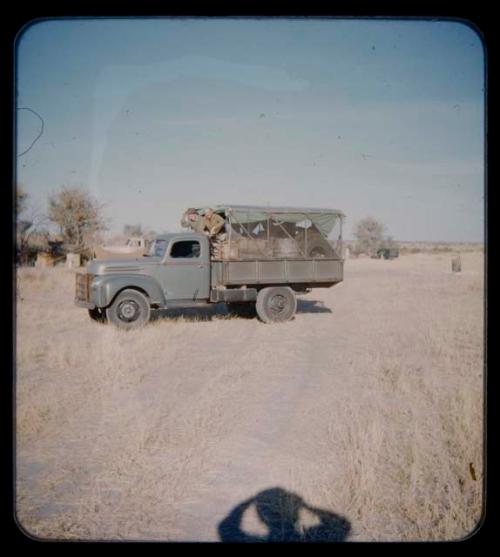 Two men leaning out of the front of an expedition truck's trailer on their trip from "Kubi"