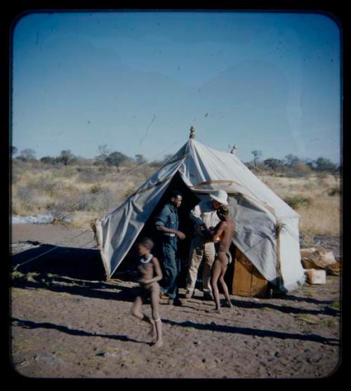 Expedition: Kernel Ledimo, Laurence Marshall, and a man standing in front of a tent, with a child running in the foreground