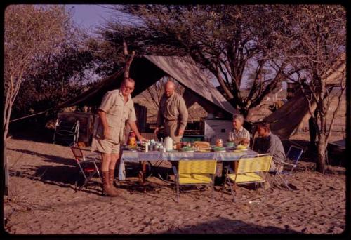 C.J. Mathias and O.P.M. Prozesky standing, with Lorna Marshall and Kurt Ahrens sitting at the expedition camp breakfast table