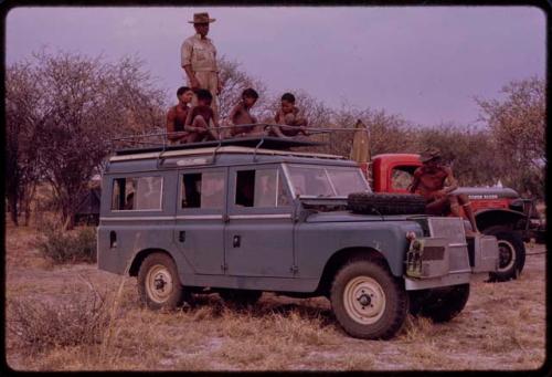 Boys sitting and Wilhelm Camm standing on the top of Land Rover, with a man sitting on the hood