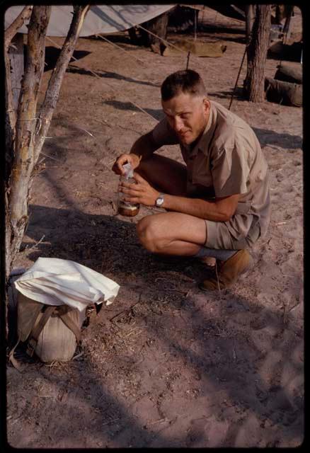 Wulf Haacke crouching and holding a jar in his hands