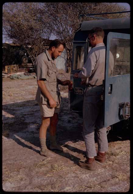 Kurt Ahrens and Nicholas England making a microphone shield, standing beside an expedition Land Rover