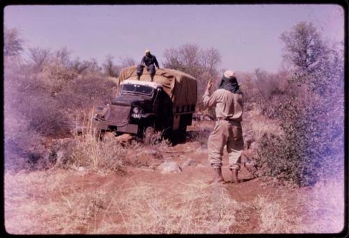 Expedition member sitting on the top of a truck, with another man standing facing him