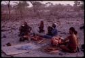 Group of people sitting on the ground  near Utukili's place and preparing meat given by Ratipa