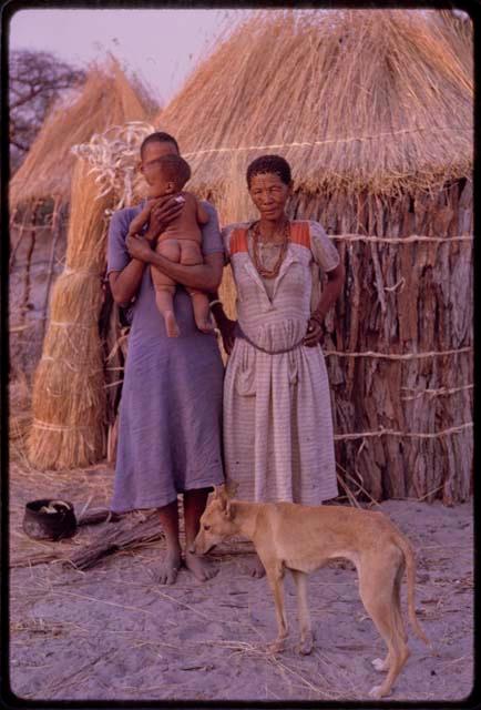 Young woman holding a baby and an elderly woman, standing in the werft of a girl who is blind, with a dog in the foreground