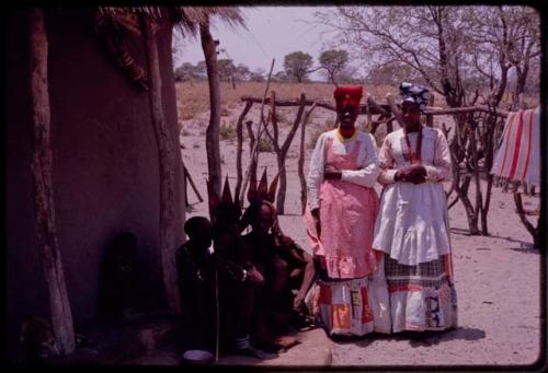 Young women wearing "modern" Herero dresses and women wearing "traditional" Herero dress (one of them is probably Thikithe, a daughter of Wareka) sitting nearby