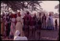 Group of women wearing "modern" Herero dress and young girls wearing "traditional" apron with strings standing to sing at Lukas' place; a well-known singer, Kandyendye, is performing