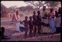 Women wearing "modern" Herero dress and young girls wearing "traditional" apron with strings standing to sing at Lukas' place