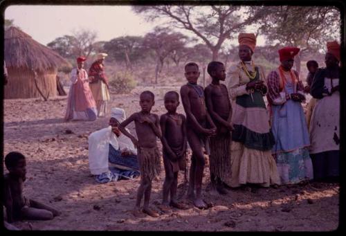 Women wearing "modern" Herero dress and young girls wearing "traditional" apron with strings standing to sing at Lukas' place