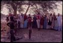 Kandyendye in a pink shirt singing, with a group of women wearing "modern" Herero dress and children