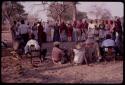 Kandyendye in a pink shirt singing, with a group of women wearing "modern" Herero dress and men sitting in chairs