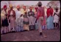 Kandyendye in a pink shirt singing, with a group of women wearing "modern" Herero dress