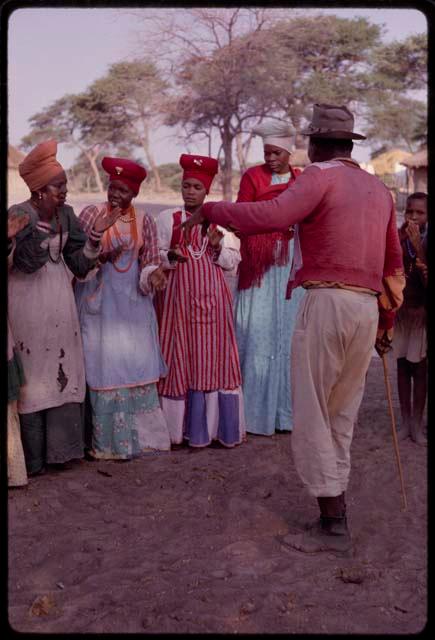 Kendyendye singing, with a group of women wearing "modern" Herero dress clapping