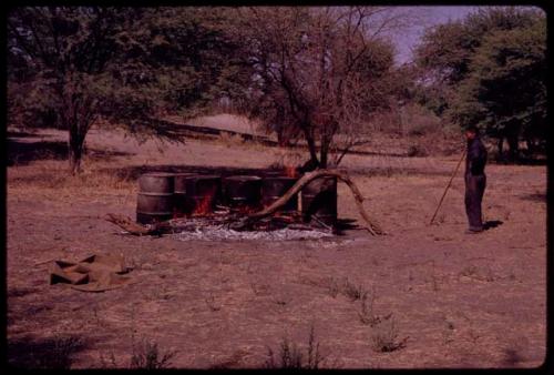 Man standing near barrels with fire built around them to boil water