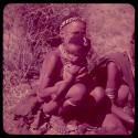 Medicine: Woman sitting and holding a child; the child has black medicine on their eyebrows