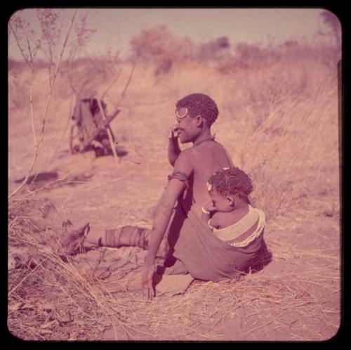 Portraits: Woman of "Gao Hunchback's" group sitting, with a child tied to her back who has a headband around her shoulders