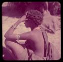 Portraits: //Kushay (wife of /Qui) wearing metal wire bracelets and yellow beads, sitting, view from behind