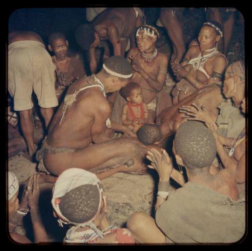 Medicine man leaning over a circle of women and children clapping at a night dance