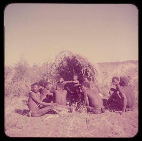 Story: Story-telling group sitting in front of a skerm, including Zuma, Gao of Band 24 (Zuma's husband), "Crooked /Qui," "Gao Medicine," and Demi