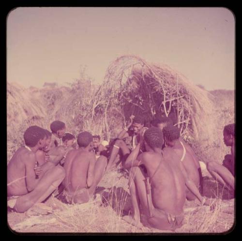 Story: Story-telling group sitting in front of a skerm, including Zuma, Gao of Band 24 (Zuma's husband), "Crooked /Qui," "Gao Medicine," and Demi