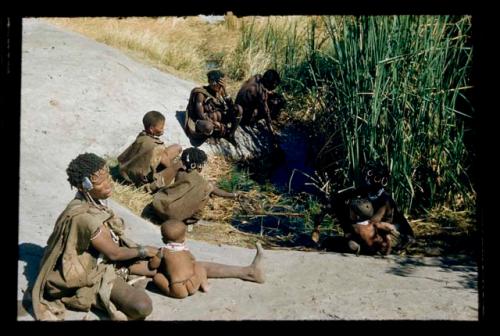 Water: Group of women and children sitting next to a waterhole, including !U with !Ungka Norna, "Little N!ai," and //Khuga