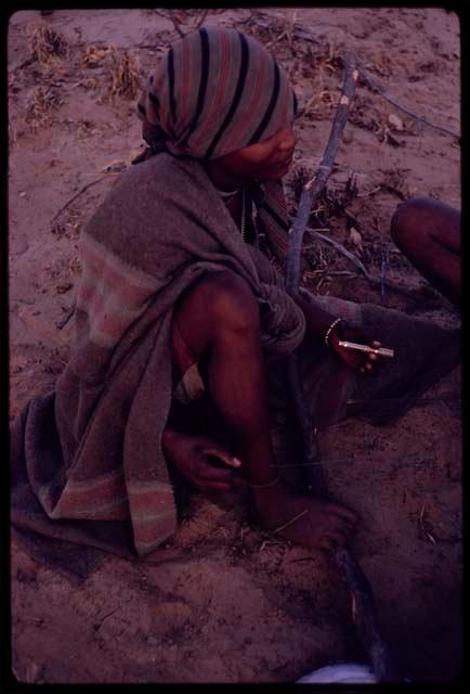 N/kxabe playing dandiri, holding a cartridge in her hand, striking the string with a little stick