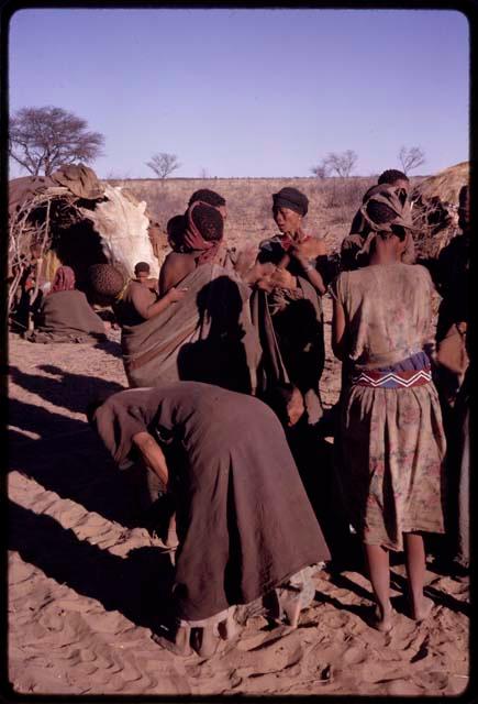 Tomku standing with other women clapping at the beginning of a social dance, view from behind