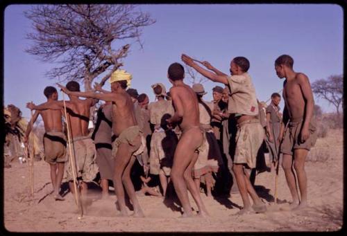 Group of men (including /'O /hei, /Gaishay, /Xoxa, !Kxam and Tama) performing a social dance in a line around a group of women standing