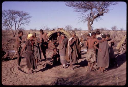 Group of people beginning to perform a social dance, including N//aba wearing a dress and yellow kerchief, Sãõ?//e, /Xoxa, and /Oβa dancing with /Gaishay