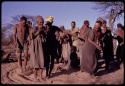 Group of people performing a social dance, with /Xoxa wearing a yellow kerchief and dancing with Sãõ?//e, N//aba in front of them, and Tama following