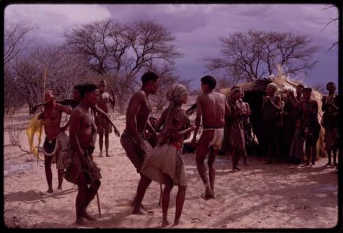 /Xoxa, N!obe, /Gaishay, Tama and N/kxabe dancing in a social dance, with a group of women singing and clapping in the background