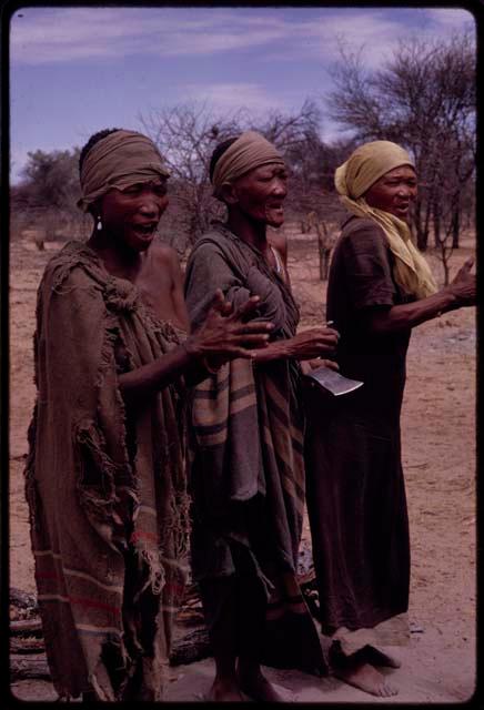 N//aba wearing a yellow kerchief, singing with Sãõ?//e and another woman at the beginning of the Eland Dance, Sãõ?//e playing an axe blade