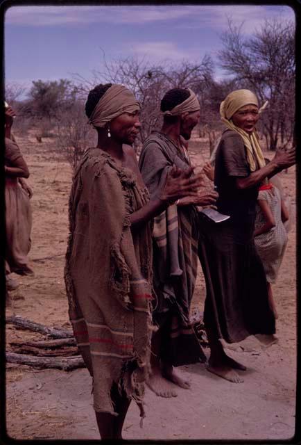 N//aba wearing a yellow kerchief, singing with Sãõ?//e and another woman at the beginning of the Eland Dance, Sãõ?//e playing an axe blade