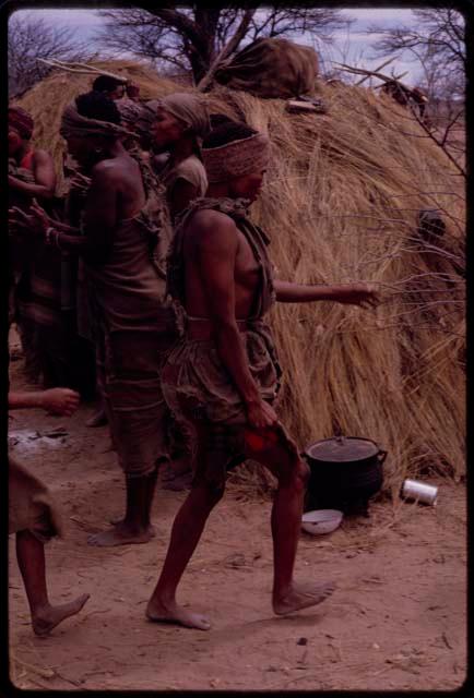 Dadum dancing in the Eland Dance, with women standing and clapping behind her