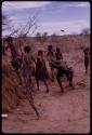 Group of people performing the Eland Dance, including Twi imitating an eland swiping at something with his horns