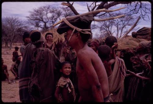 !Kxam wearing horns tied to his head in the Eland Dance, with a group of people standing behind him