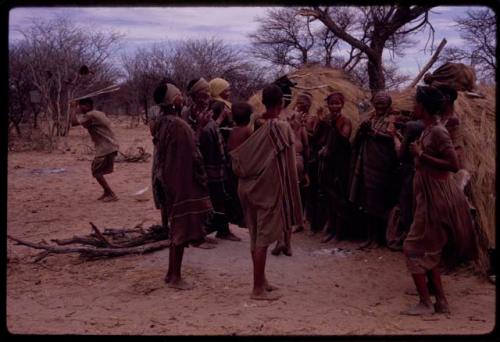 Group of people performing the Eland Dance in front of a skerm, including women dancing, singing and clapping, with Twi wearing horns on his head, dancing in the background