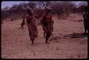 !Kxam wearing horns on his head, dancing in the Eland Dance, followed by !Ani and an unidentified man wearing horns