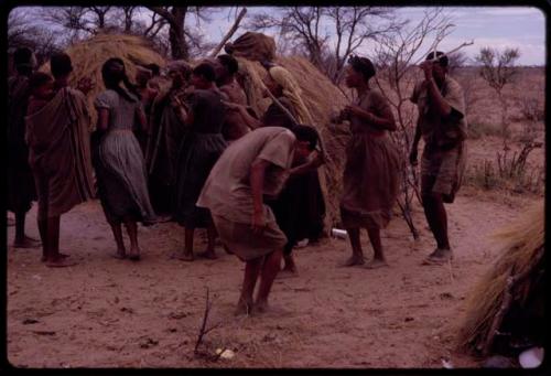 Group of people performing the Eland Dance in front of a skerm, including Twi holding horns to his head and imitating the motions of an eland