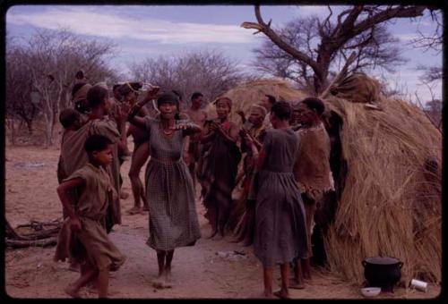 Group of women performing the Eland Dance in front of a skerm, with ≠Kxoba dancing in the center of a circle of women standing and clapping