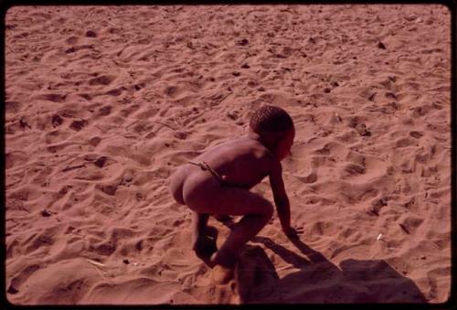 Child crouching in the sand, seen from behind