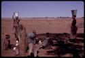 Women holding their buckets on their heads while others sit and fill ostrich eggshells with water