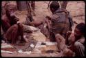 Dadum sitting on animal skins and smoking while her husband (Tama) sews with a boy sitting behind him