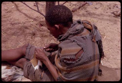 Tama sitting and sewing, showing how he makes a hole with an awl for the thread to go through, close-up