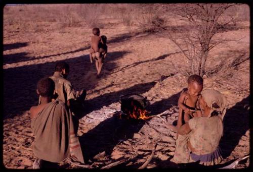 Tomku sitting and holding her baby, with other people and children, seen from behind