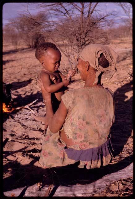 Tomku sitting in the sand and holding her baby, seen from behind