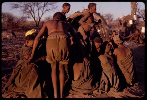 /Xoxa and /Gaishay performing a curing dance around a group of women sitting in a circle while /'O/hei/ bends over to cure one of the women in the foreground