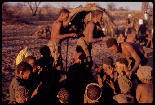 /Xoxa and /Gaishay performing a curing dance around a group of women sitting in a circle and clapping while /'O/hei/ bends over to cure one of the women